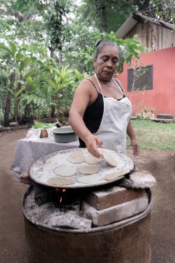 Yaşlı bir İspanyol kadın, Guatemala 'nın doğasında açık hava sobası üzerinde geleneksel mısır tortillası pişiriyor. Yerel gıda konsepti