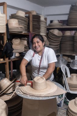 An adult Hispanic woman is smiling while working in a hat traditional workshop in Guatemala clipart