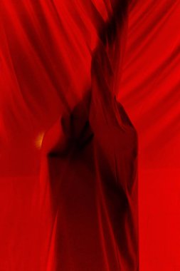 Gecenin karanlığında apartmanın karanlık balkonunda dikilirken kırmızı şeffaf ışık perdelerinin arkasında saklanan tanımlanamayan gizemli kişi.