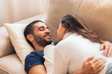 Evlerinde rahat bir kanepede oturan genç bir erkekle kadın arasında romantik bir anı yakalayan güzel bir fotoğraf. Çift birbirine sırılsıklam aşık görünüyor.