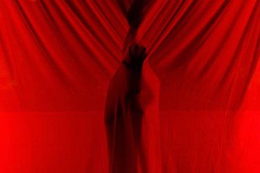 Gecenin karanlığında apartmanın karanlık balkonunda dikilirken kırmızı şeffaf ışık perdelerinin arkasında saklanan tanımlanamayan gizemli kişi.