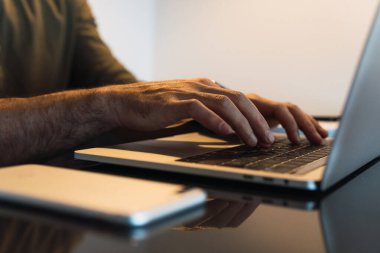 Çalışma sırasında aydınlatma odasında akıllı telefonlu bir masada otururken modern taşınabilir ağ kitabına göz atan isimsiz bir erkek çalışanı kırpın