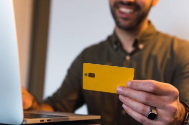 Plastik kredi kartıyla tanınmayan, tanınmayan, pozitif sakallı bir erkek. Aydınlatma odasındaki masada, internet üzerinden ödeme yapıyor.