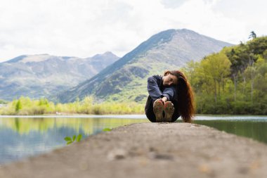 Pirenes Dağı 'ndaki göletin yanındaki taş rıhtımda oturan kadın yürüyüşçü kameraya bakıyor.