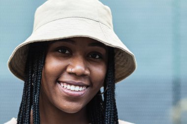 Yazlık şapkalı, şık örgülü ve kameraya bakan genç bir Afro-Amerikan kadın.