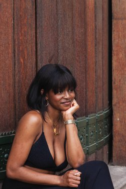 Afro-Amerikan zevkli bir kadın ahşap duvarın karşısında dikilip başka tarafa bakıyor.