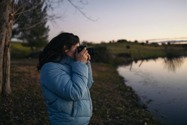 Genç fotoğrafçı kadın doğada güzel bir gölün günbatımı fotoğraflarını çekiyor..