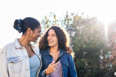 İki Latin Amerikalı arkadaş sokakta yürüyor, eğleniyor ve akıllı telefon kullanarak gülüyorlar..