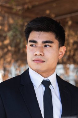 Ciddi etnik erkek girişimci şık bir takım elbise giyiyor. Güneşli bir günde gölgede dikiliyor ve gözlerini kaçırıyor.