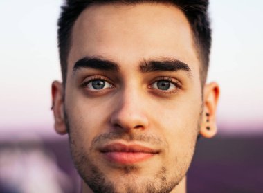 Gün batımında lavanta tarlasında ciddi bir ifadeyle kameraya bakan mavi gözlü genç bir adamın portresi.