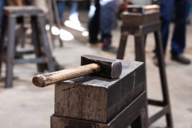 Demir ocağındaki tezgahta ahşap saplı ağır metal başlı bir alet.