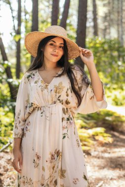 Hasır şapkalı güzel esmer kadın ormanda yürüyor.