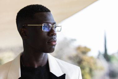 Şık ceketli genç, kendine güvenen siyahi girişimci şehirde kameraya bakıyor.