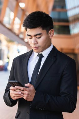 Keyifli Asyalı işadamı sokakta duruyor ve cep telefonuyla internette sörf yapıyor.