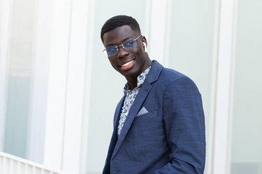 Tarz sahibi Afrikalı Amerikalı erkek girişimci şehir merkezinde dikilip gözlerini kaçırırken kablosuz kulaklıkla müzik dinliyor.