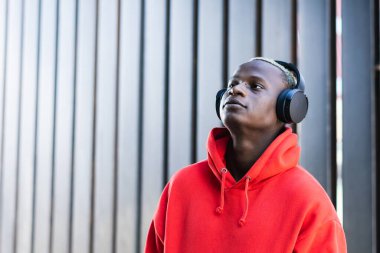 Moda kapüşonlu genç Afrikalı Amerikalı erkek melodinin yan görüntüsü. Kablosuz kulaklıkla şarkıların tadını çıkarıyor.