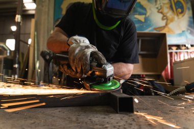 Elektrikli öğütücü kullanan ve pis atölyedeki metal parçalarını kesen koruyucu şapkalı tanımlanamayan erkek kaynakçı.