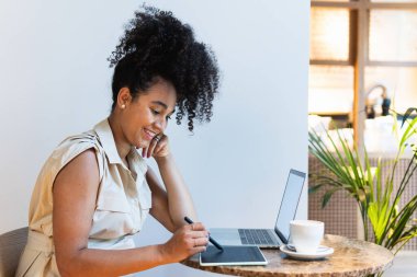 Masada dizüstü bilgisayarlı ve kahveli grafik tablet kullanan Afro-Amerikalı serbest kadın.