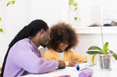 Gülümseyen Afrikalı Amerikalı baba okula hazırlanırken kız internet sitesiyle masada oturuyor.