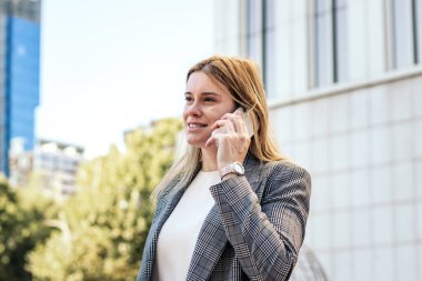 Takım elbiseli bir iş kadını ofisten çıkarken telefonda konuşuyor.