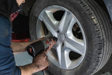 Otomatik tornavida kullanan isimsiz erkek tamirci garajda araba bakımı sırasında tekerlek değiştirirken...