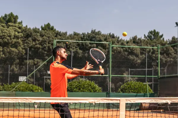 Spor giyimli bir adam tenis kortunda tenis oynuyor. Onu bir tenis kulübünde eğitmeye odaklanmış..