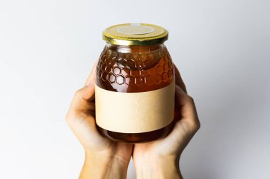 Beyaz arka planda cam kavanozda doğal sıvı bal bulunan tanınmamış bir ekin insanı.