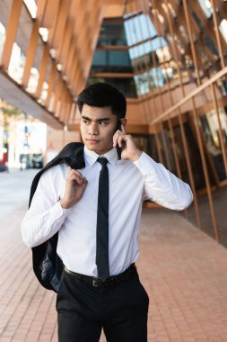 Siyah takım elbiseli neşeli erkek girişimci modern binanın yanındaki merdivenlerde duruyor ve cep telefonuyla iş konularını tartışıyor.