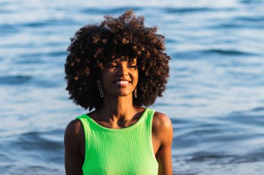 Mayo giymiş, kıvırcık saçlı ve yaz tatilinde eğlenen neşeli Afro-Amerikan kadın.