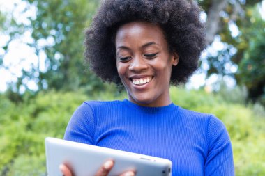 Parkta bankta oturan ve yeni başlatılan projede çalışırken tablet kullanan içerikli Afrikalı Amerikalı kadın serbest yazar