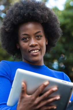 Parkta bankta oturan ve yeni başlatılan projede çalışırken tablet kullanan içerikli Afrikalı Amerikalı kadın serbest yazar