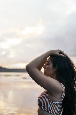Kosta Rika 'da güzel bir sahilde duran uzun saçlı esmer kadın gün batımını izliyor.