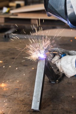 Koruyucu eldivenli, tanınmayan kaynakçının yukarısından atölyedeki eski püskü tezgahta metal parçaları kaynatıyordu.