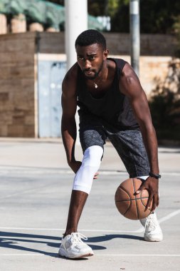 Kararlı Afrikalı Amerikalı erkek sporcu yazın sahada basketbol oynuyor.
