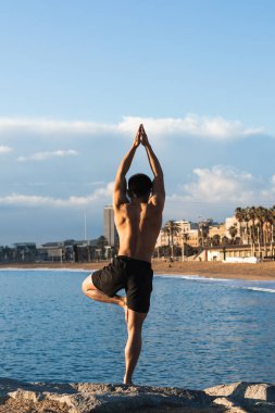 Gömleksiz, kaslı bir erkeğin, şehir limanındaki yoga oturumunda farklı pozlar vermesi.
