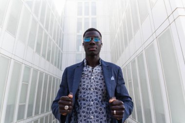 Düşük açılı Afrikalı Amerikalı erkek girişimci şehir merkezinde durup kameraya bakarken kablosuz kulaklıkla müzik dinliyor.