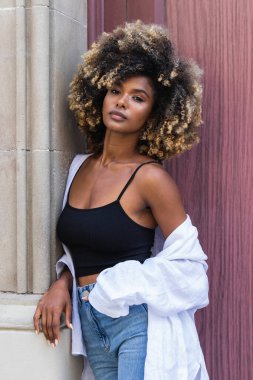 Kendine güvenen Afro-Amerikan kadın şık giyinmiş renkli kapıya bakan kameraya bakıyor.