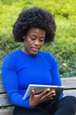 Afro-Amerikalı kadın serbest çalışan park bankında oturuyor ve başlangıç projesinde çalışırken tablet kullanıyor.