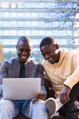 Parkta boş zaman geçirirken internet üzerinden internette gezinen Afro-Amerikalı olumlu erkek arkadaşlar
