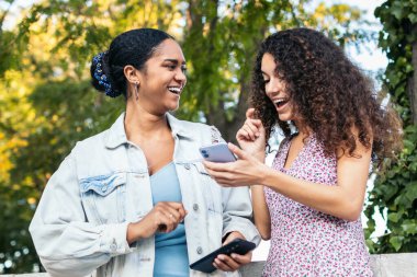 İki Latin Amerikalı arkadaş sokakta yürüyor, eğleniyor ve akıllı telefon kullanarak gülüyorlar..