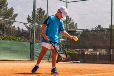 Spor giyim ve şapkalı küçük bir çocuk tenis kortunda tenis oynarken elinden gelenin en iyisini yapmaya çalışıyor.