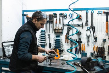 Otomotiv ustası, garajda çeşitli aletlerle çalışırken İngiliz anahtarıyla motorsiklet krank milinin bir kısmını vidaladığını yan görüyor.