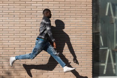 Şehirde gölgeyle birlikte duvarın yanında koşan alelacele koşan sıradan bir adam.