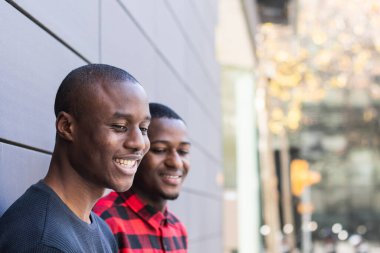 Mutlu Afrikalı Amerikalı arkadaşlar, gri duvara yaslanıp kameraya bakıyorlar.