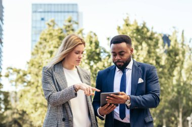 Ofis kıyafetleri içindeki işadamları tablet kullanarak şirket verileri hakkında konuşuyorlar.