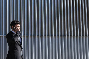 Siyah takım elbiseli neşeli erkek girişimci modern binanın yanındaki merdivenlerde duruyor ve cep telefonuyla iş konularını tartışıyor.