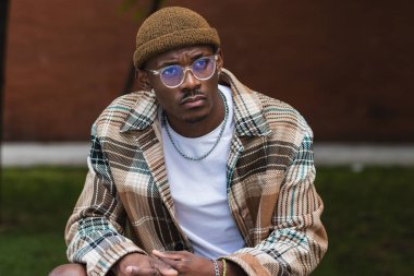 Moda desenli tişörtlü genç siyahi adam modern şehrin sokaklarında serinlerken kaşlarını çatıyor ve yüzünü çeviriyor.