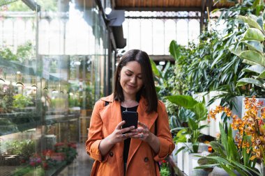 Bahçe merkezinde cep telefonu kullanan memnun bir kadın.