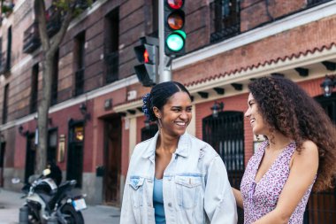 İki kız yaya geçidinde trafik ışığının yayalar için yeşile dönmesini bekliyor. Konuşuyorlar, gülüyorlar, şehirde günün tadını çıkarıyorlar..