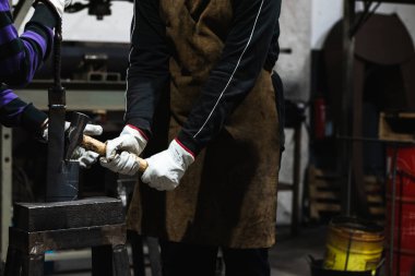 Metal rafta duran ve demir ocağında çekiçle vurulan isimsiz bir işçi ve meslektaşı.